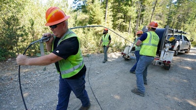 Carl Roath, left, a worker with the Mason County (Wash.) Public Utility District, pulls fiber optic cable off of a spool, as he works with a team to install broadband internet service to homes in a rural area surrounding Lake Christine near Belfair, Wash., on Aug. 4, 2021. Federal officials announced plans Thursday, July 28, 2022, to spend $401 million in grants and loans to expand the reach and improve the speed of internet for rural residents, tribes and businesses in 11 West and Central U.S. states.