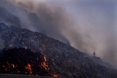 A person picks through trash for reusable items as a fire rages at the Bhalswa landfill in New Delhi, April 27, 2022. Landfills are releasing far more planet-warming methane into the atmosphere from the decomposition of waste than previously thought, a study suggests. Smoke hung over New Delhi for days after the massive landfill caught fire as the country was sweltering in an extreme heat wave.