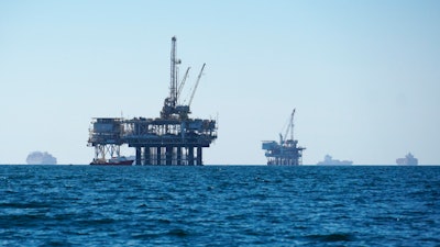 Cargo vessels are anchored offshore near oil platforms, before heading into the Los Angeles-Long Beach port on Oct. 5, 2021. The first official federal calculations of the new spending package that President Biden signed show it will slice America's carbon pollution by more than 1 billion tons by the end of the decade. The new law’s provisions that call for oil and gas leasing on federal land and water “may lead to some increase” in carbon pollution, the federal analysis said.