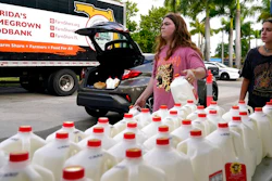 Vanessa Correa, left, and Gigi Fiske, right, pass out gallons of milk at a food distribution held by the Farm Share food bank, Wednesday, July 20, 2022, in Miami. Long lines are back at food banks around the U.S. as working Americans overwhelmed by inflation turn to handouts to help feed their families.