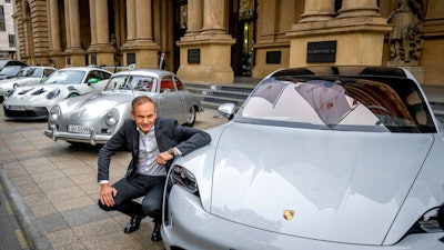 CEO of Porsche car maker Oliver Blume kneels next to Porsche cars at the start of Porsche's market listing at the stock market in Frankfurt, Germany, Thursday, Sept. 29, 2022.