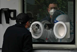 A man wearing face mask waits in line as a worker in protective suit collects a sample from a man at a coronavirus testing site in Beijing, Wednesday, Nov. 9, 2022.