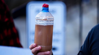 Craig Stevens holds a bottle of brown water as he speaks with members of the media outside the Susquehanna County Courthouse in Montrose, Pa., Tuesday, Nov. 29, 2022. Pennsylvania's most active gas driller has pleaded no contest to criminal environmental charges in a landmark pollution case. Houston-based Coterra Energy Inc. entered its plea Tuesday.