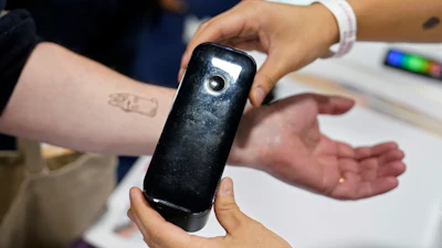 An exhibiter apples a temporary tattoo with a Prinker digital temporary tattoo device during CES Unveiled before the start of the CES tech show, Tuesday, Jan. 3, 2023, in Las Vegas. The device allows the user to print a temporary tattoo in cosmetic ink.