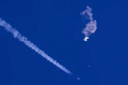 In this photo provided by Chad Fish, the remnants of a large balloon drift above the Atlantic Ocean, just off the coast of South Carolina, with a fighter jet and its contrail seen below it, Saturday, Feb. 4, 2023.