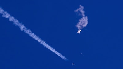 In this photo provided by Chad Fish, the remnants of a large balloon drift above the Atlantic Ocean, just off the coast of South Carolina, with a fighter jet and its contrail seen below it, Saturday, Feb. 4, 2023.