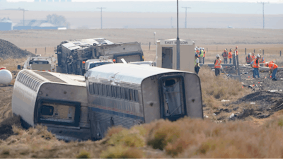 Workers stand near train tracks, Sept. 27, 2021, next to overturned cars from an Amtrak train that derailed a few days prior near Joplin, Mont., killing three people and injuring others.