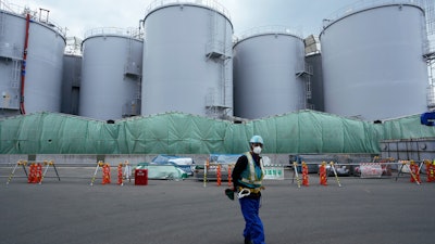 A worker helps direct a truck driver as he stands near tanks used to store treated radioactive water after it was used to cool down melted fuel at the Fukushima Daiichi nuclear power plant, run by Tokyo Electric Power Company Holdings (TEPCO), in Okuma town, northeastern Japan, on March 3, 2022.