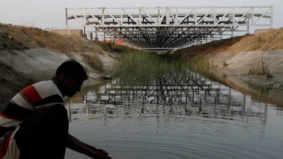 A worker washes his hands as installed solar panels are visible atop the Narmada canal at Chandrasan village, outside of Ahmadabad, India, Feb. 16, 2012.