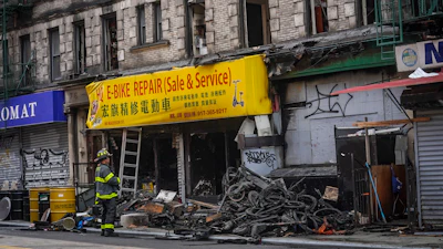 A firefighter looks through debris in the aftermath of a fire which authorities say started at an e-bike shop and spread to upper-floor apartments, Tuesday June 20, 2023, in New York.