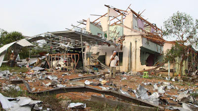People speak on their phones in front of a house damaged by an explosion at a firework warehouse in Narathiwat province southern Thailand Saturday, July 29, 2023.