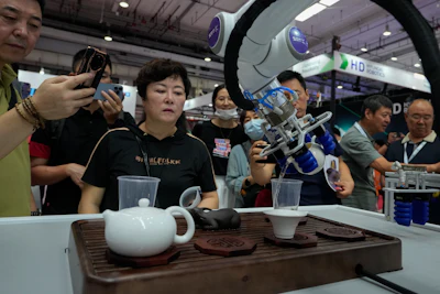 Visitors look at a robotic arm performs a Chinese tea serving during the annual World Robot Conference at the Etrong International Exhibition and Convention Center on the outskirts of Beijing, Thursday, Aug. 17, 2023.