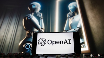 The OpenAI logo is displayed on a cell phone with an image on a computer monitor generated by ChatGPT's Dall-E text-to-image model.