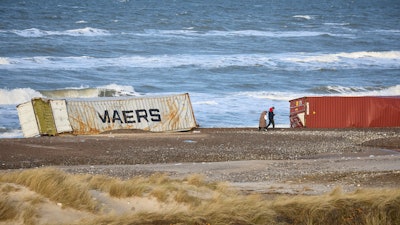 People walk past stranded containers in the area between Tranum and Slette beach in Denmark, Saturday, Dec. 23, 2023, a day after a Maersk ship dropped 46 containers off the coast between Bulbjerg and Svinkloev in the northwestern part of Jutland, during storm Pia.