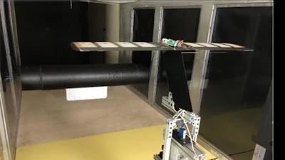 A large black cylinder with a plate attached at the front creates irregular turbulence under the tunnel's high-speed winds. The airfoil wing system with eight pressure sensors and a pitot tube is mounted on a load cell to measure the lift experienced by the system.
