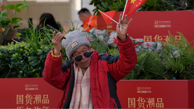 A man waves the Chinese national flag and Communist Party flag in the popular Wangfujing shopping street in Beijing, China, Thursday, March 6, 2025.
