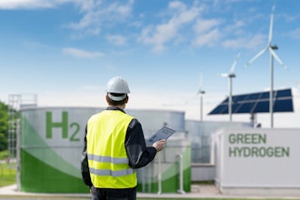 Worker in safety vest inspecting green hydrogen production facility with solar and wind energy.