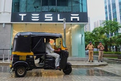 Policemen stand guard as a three-wheeler auto-rickshaw drives past India's first Tesla showroom to be inaugurated in Mumbai, India, Tuesday, July 15, 2025.
