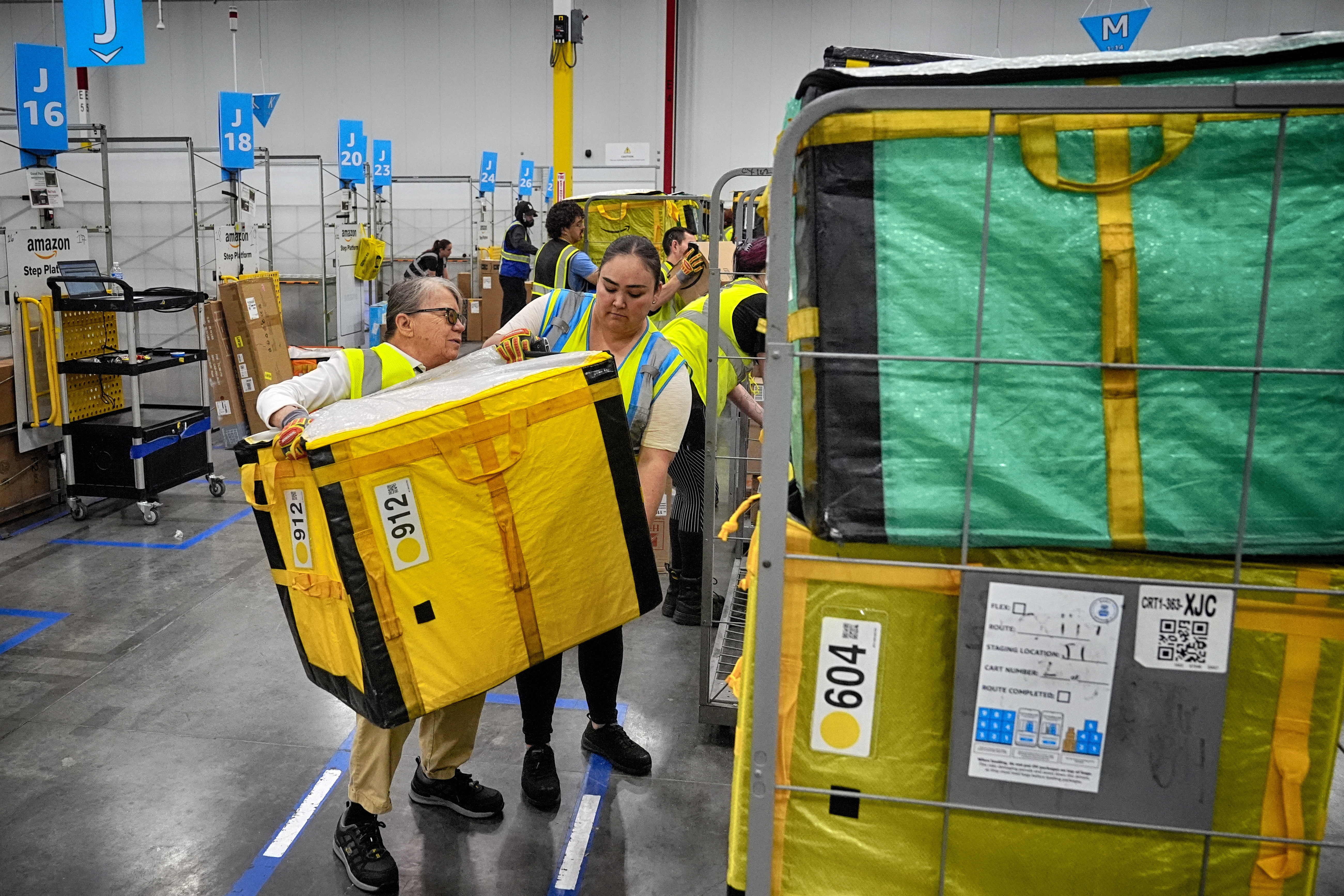 Amazon employees load packages on carts at Amazon's DAX7 delivery station, July 16, 2024, South Gate, Calif.