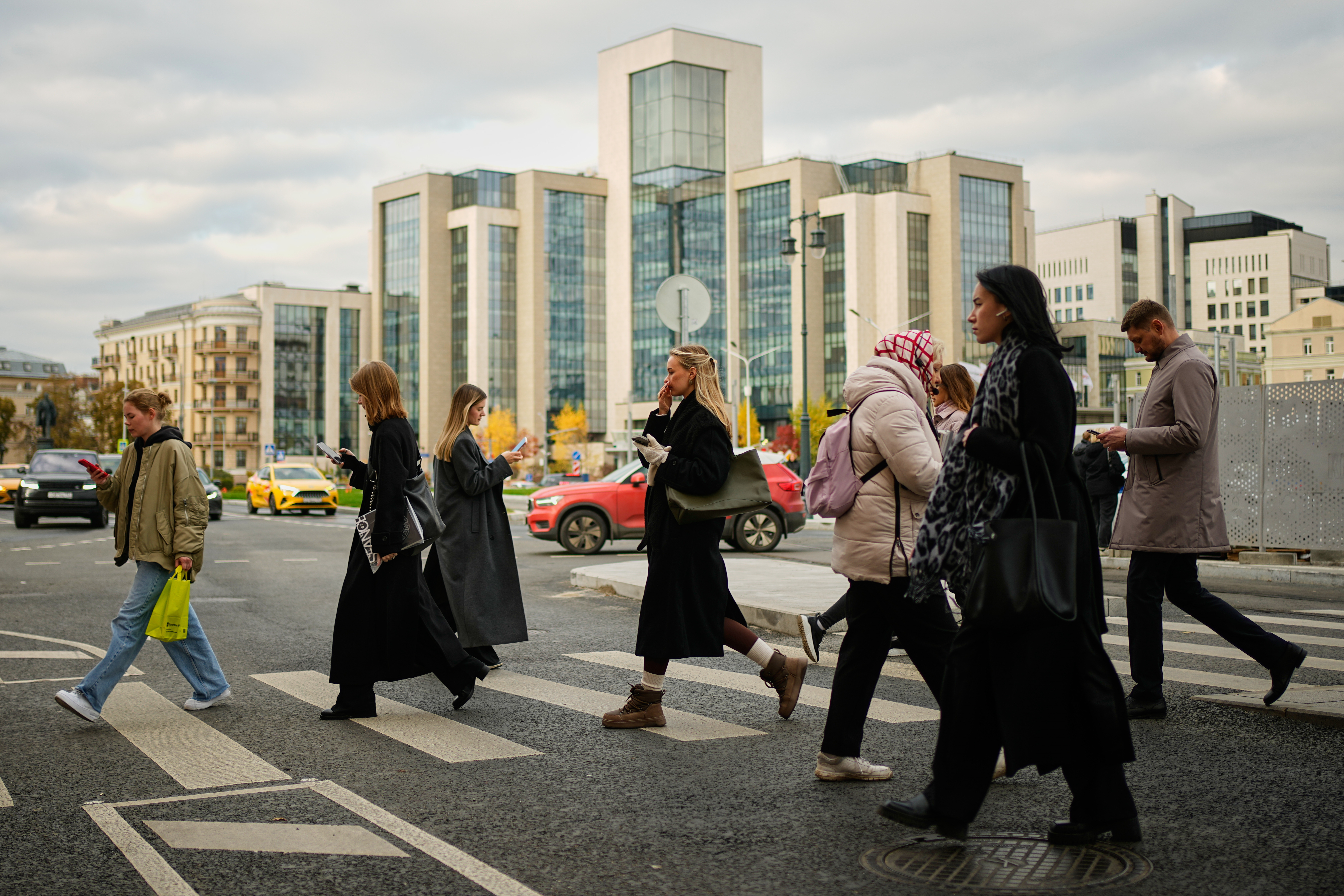 People cross a street, with Russian oil company Lukoil's headquarters seen in the background, in Moscow, Russia, Thursday, Oct. 23, 2025.