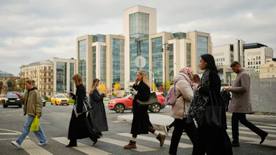 People cross a street, with Russian oil company Lukoil's headquarters seen in the background, in Moscow, Russia, Thursday, Oct. 23, 2025.
