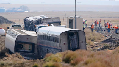 In this Sept. 27, 2021, file photo, workers stand near train tracks next to overturned cars from an Amtrak train that derailed near Joplin, Mont.