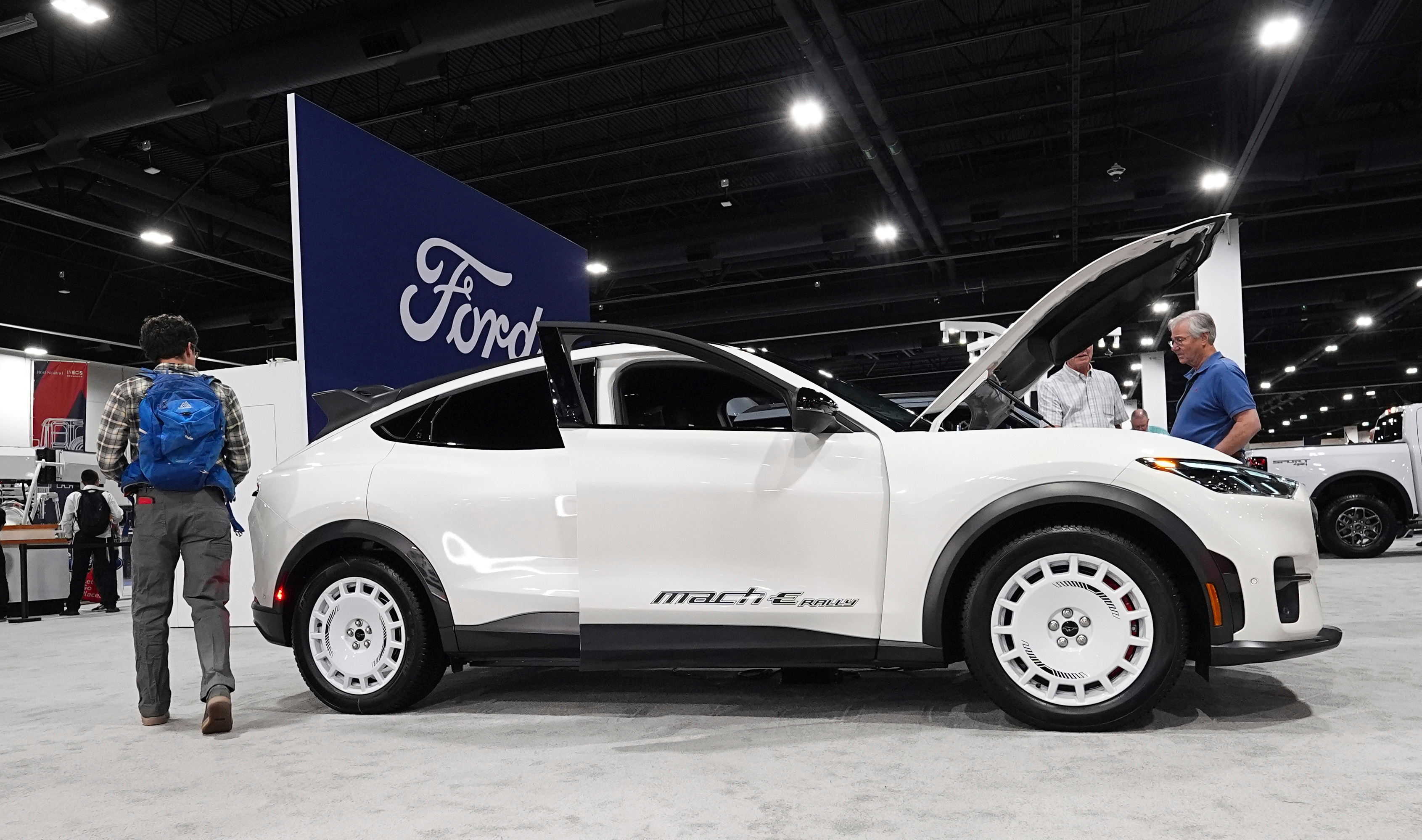 Shoppers look over a 2025 Mach-E electric utility vehicle in the Ford display at the Colorado Auto Show, April 17, 2025, in Denver.