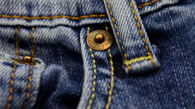 Close-up of a brass button on blue denim with yellow stitching detail