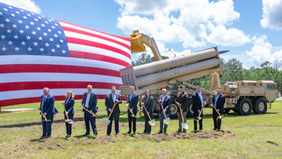 Military officials conduct groundbreaking ceremony with shovels before American flag and equipment