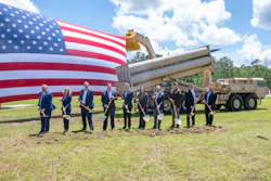 Military officials conduct groundbreaking ceremony with shovels before American flag and equipment