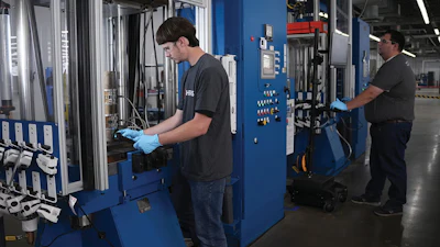 Workers operating industrial machinery in a manufacturing facility with blue equipment and control panels