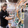 Female technician in safety glasses working on electrical panel with orange and blue wiring in industrial facility