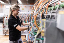 Female technician in safety glasses working on electrical panel with orange and blue wiring in industrial facility