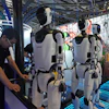 A worker reacts near a line of humanoid robots displayed at the World AI Conference in Shanghai, Friday, July 17, 2026.