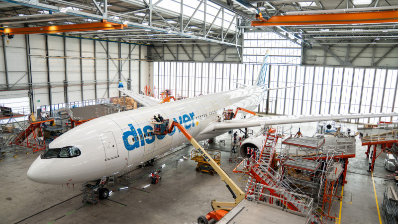 Flydubai aircraft undergoing maintenance in industrial hangar with orange support equipment and scaffolding