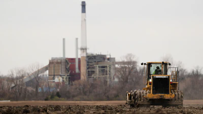 A worker prepares a plot of land for an AI data center, with a retired power plant being refurbished to provide electricity for the facility in the distance, March 24, 2026, in Independence, Mo.