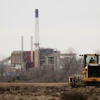 A worker prepares a plot of land for an AI data center, with a retired power plant being refurbished to provide electricity for the facility in the distance, March 24, 2026, in Independence, Mo.