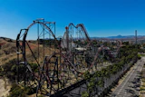 Aerial view of a steel roller coaster with red tracks winding through desert landscape and mountains in background