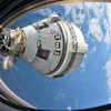Boeing Starliner spacecraft docked to International Space Station above Earth with blue sky and clouds visible
