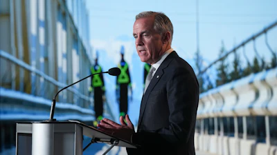 Professional man speaking at podium during outdoor event with construction workers and modern buildings in background