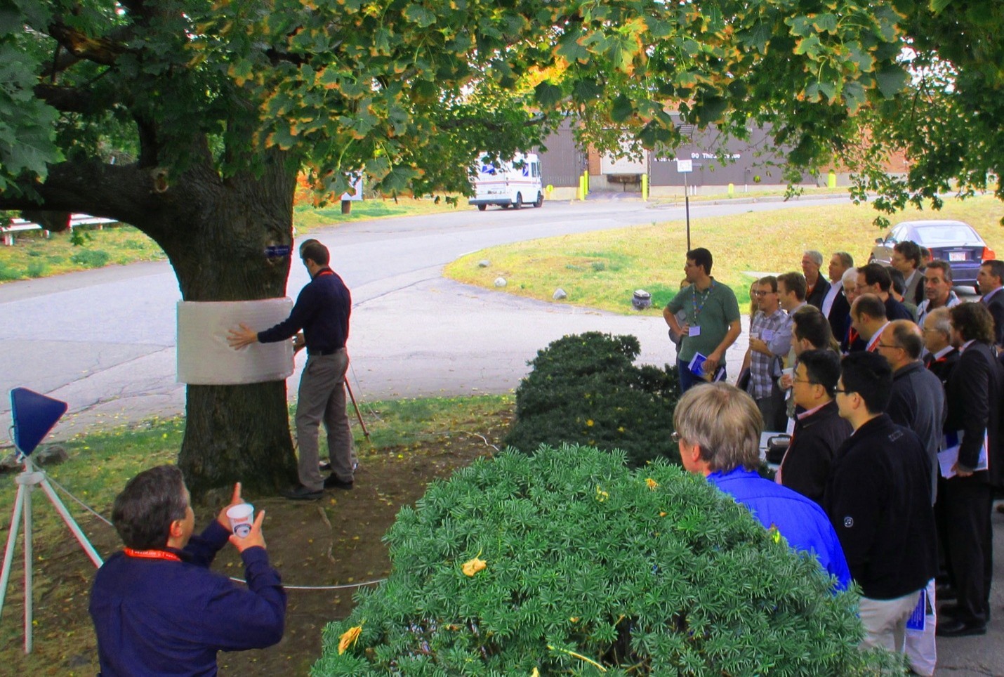 Public demonstration of a large invisibility cloak, showing the cloaking structure being positioned around a tree before an audience. This demonstration, where this portion of the tree disappeared at microwaves, was arranged and witnessed by radar boffin Dr. Eli Brookner and the IEEE Phased Array Conference participants.