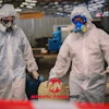 Two industrial workers in white protective suits and respirators at a manufacturing facility with Manufacturing Now logo
