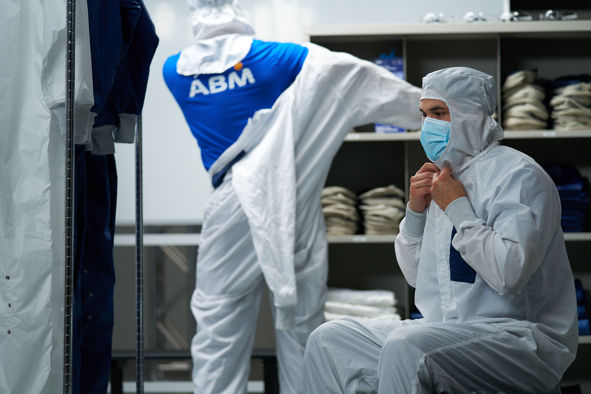 Worker in white protective suit and mask in industrial facility with shelved products and ABM branded clothing visible