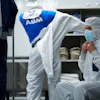 Worker in white protective suit and mask in industrial facility with shelved products and ABM branded clothing visible