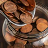 Copper pennies pouring into a glass jar for savings and financial planning