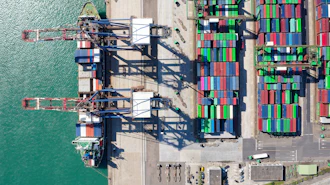 Aerial view of shipping port with cargo cranes, stacked containers, and docked vessel at waterfront terminal