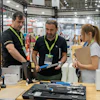 Trade show booth demonstration with staff and visitors examining tools and equipment at an industrial exhibition