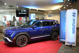 Blue Hyundai Kona electric vehicle displayed in modern showroom with branded signage and red carpet