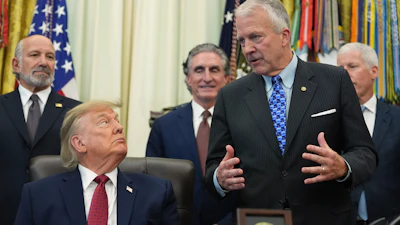 Formal meeting in the Oval Office with government officials and American flags in background