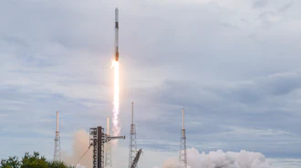 SpaceX Falcon 9 rocket launches from coastal launch pad with bright engine flames and white smoke clouds against cloudy sky